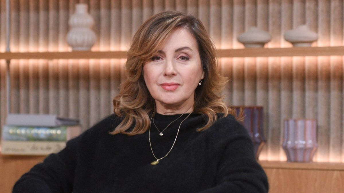 Edyta Bartosiewicz pozuje do zdjęcia we wnętrzu, patrząc w stronę obiektywu. Artystka ma na sobie czarny sweter oraz delikatną biżuterię, a w tle widoczne są drewniane półki z książkami i dekoracyjnymi naczyniami. Zdjęcie wykonano w jasnym, nowoczesnym pomieszczeniu z ciepłym oświetleniem.